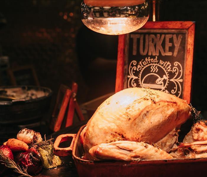 Stuffed cooked turkey in a roasting pan displayed on a table with fresh vegetables next to the turkey
